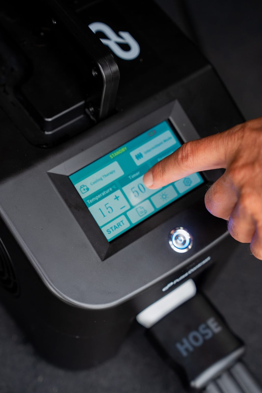 A finger setting the machine touchscreen, showing cooling therapy at 15 degrees on a 50 minute timer