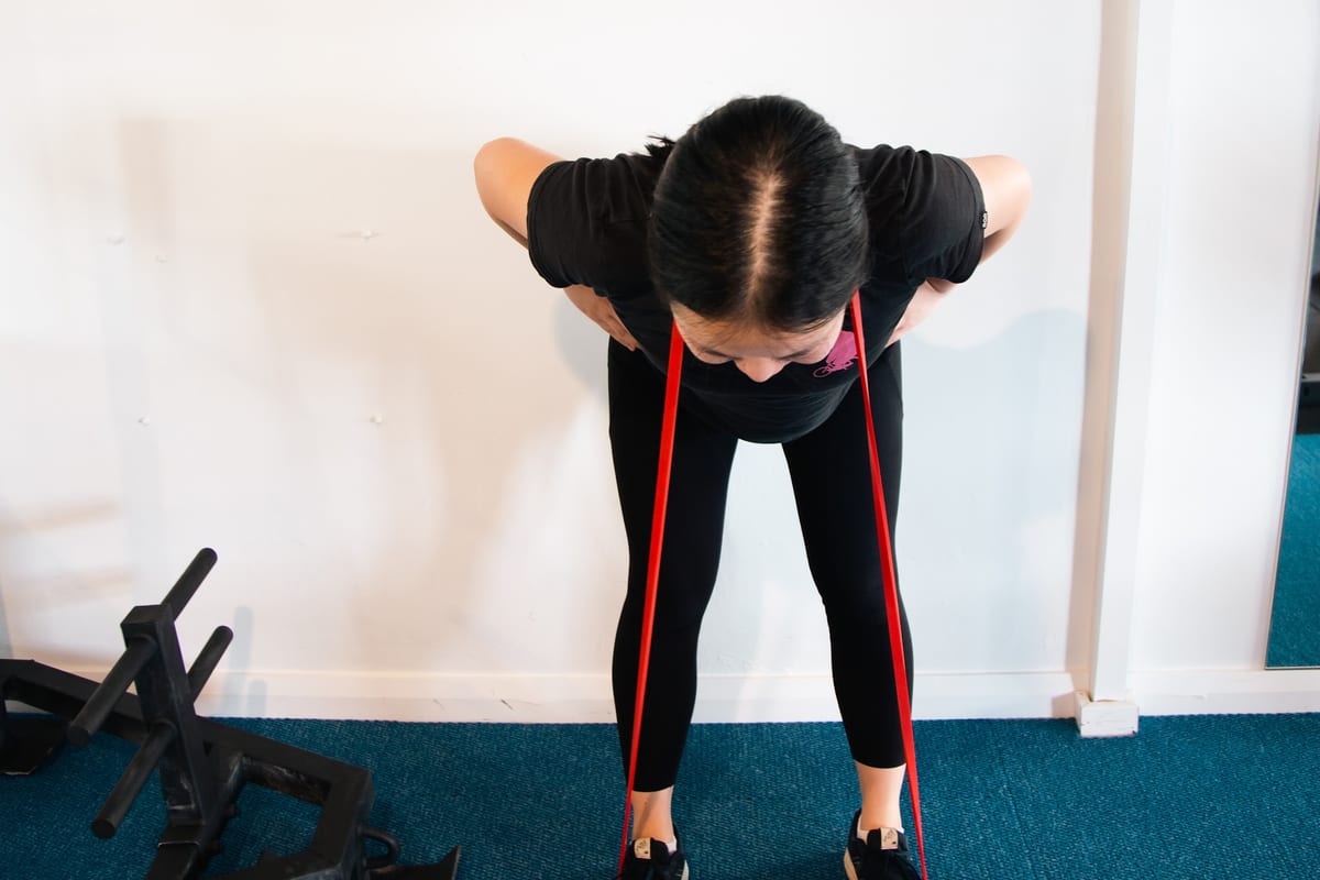 Bent-over band row for the shoulder blade muscles, SportsFit logo on the wall behind