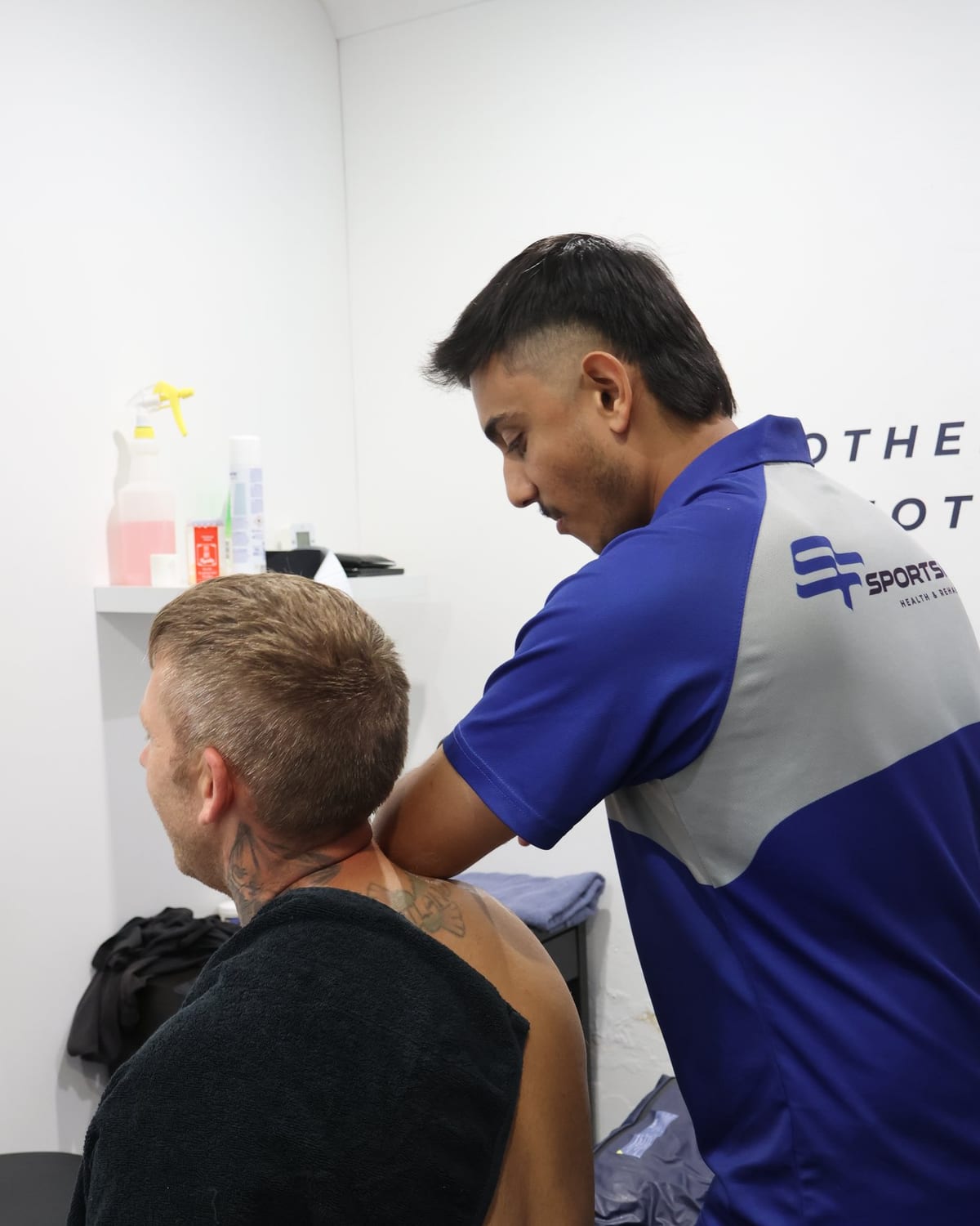 Physiotherapist treating a seated patient through the neck and upper trapezius, towel over the shoulders