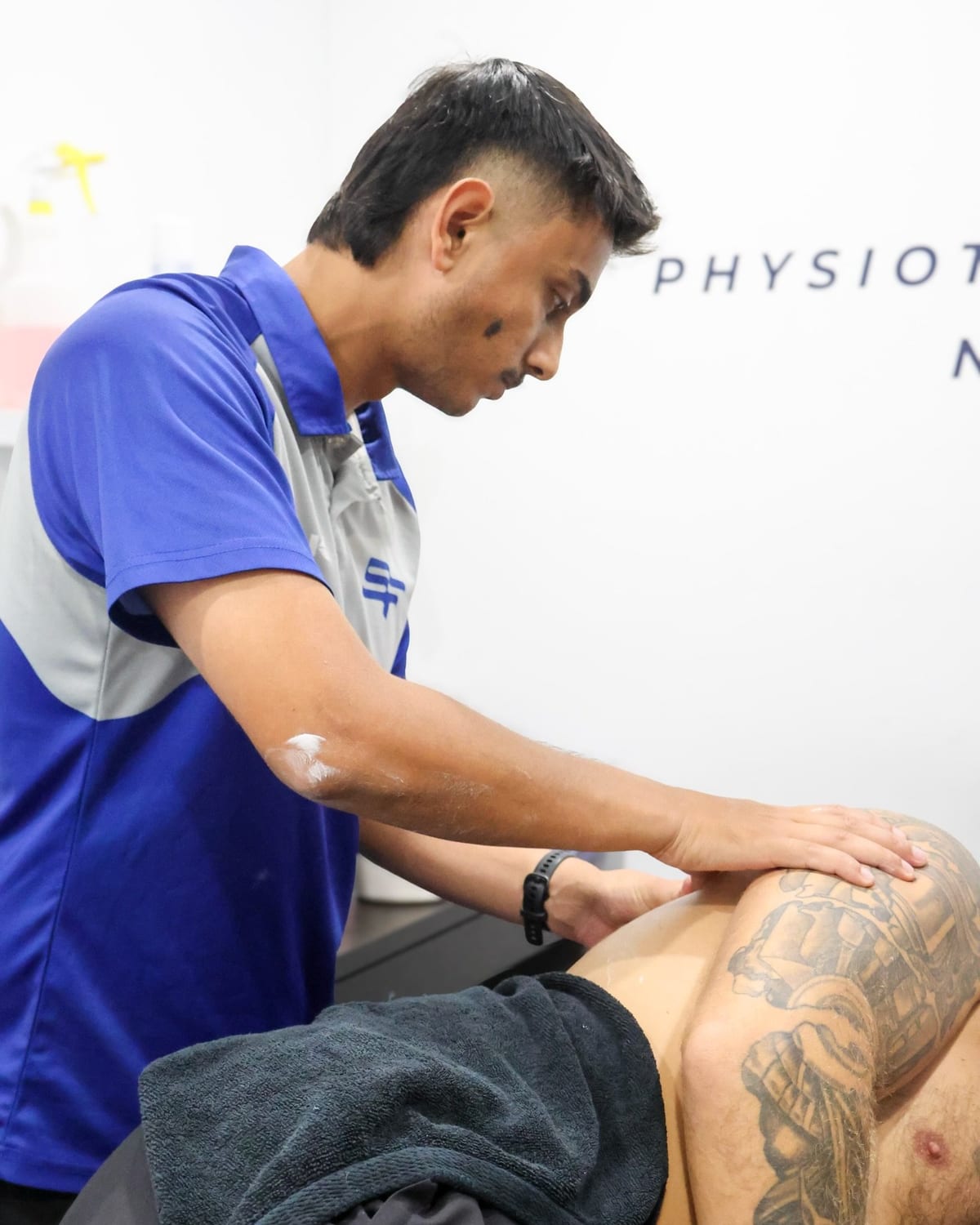 Physiotherapist applying soft tissue work along a patient shoulder and upper arm on the plinth